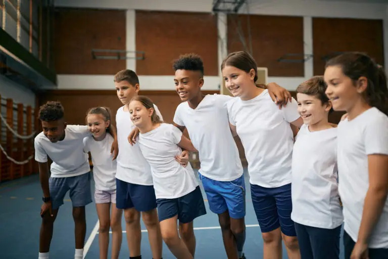Group of happy school kids standing embraced as a team during physical education class at elementary school.